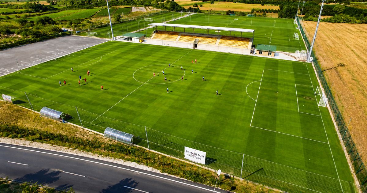 Aerial view of football training complex with players on the pitch surrounded by countryside, Side
