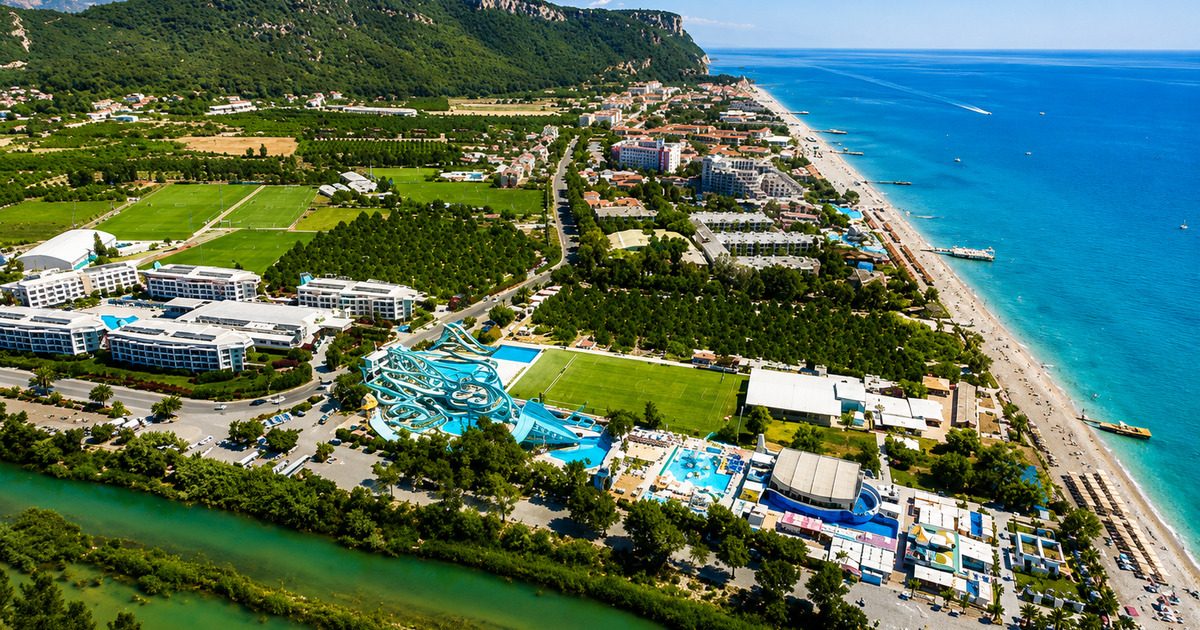 Aerial view of Kemer resort with football pitches, Mediterranean coastline and mountains in the background