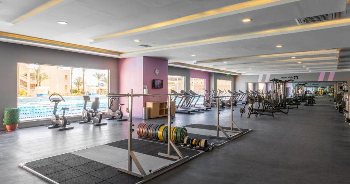 Resort gym floor with Olympic lifting platforms, coloured weight plates, barbells, and cardio machines overlooking the outdoor pool, Hurghada