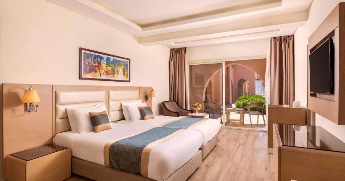 Standard double room with twin beds pushed together, warm wooden furnishings, wall art, and sliding doors opening onto a terrace, Hurghada resort