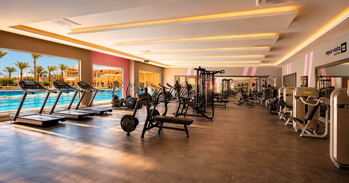 Spacious resort gym interior with cardio machines, cable stations and free weights, overlooking the outdoor Olympic pool, Hurghada