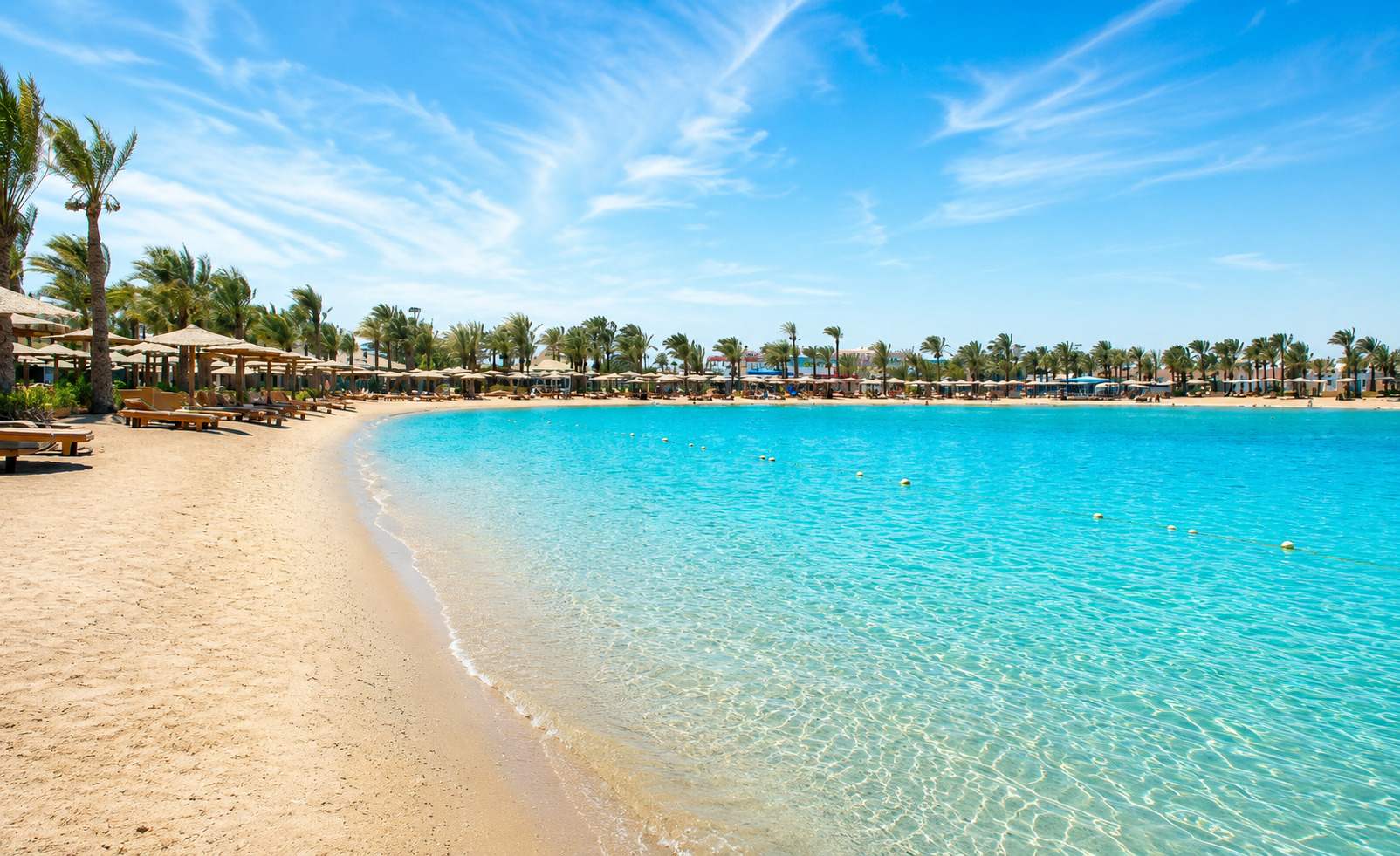 Turquoise lagoon beach with sun loungers and palm trees at a Red Sea resort in Hurghada, Egypt