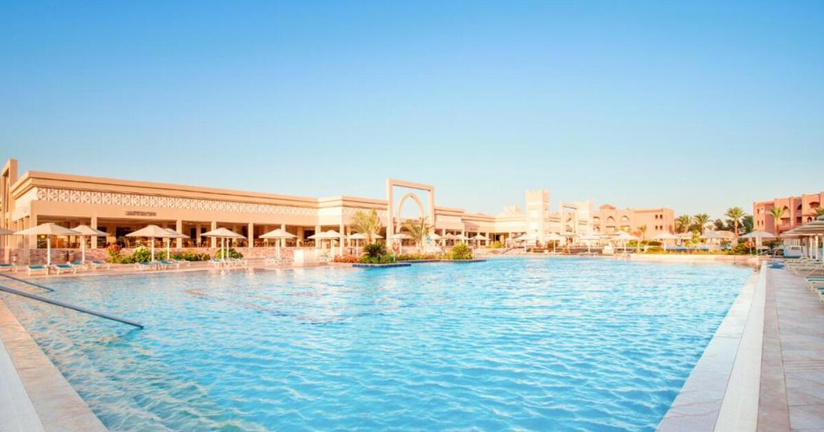 Wide resort pool at golden hour with Moorish archway entrance and main restaurant building in the background, Hurghada
