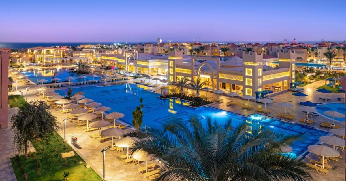 Aerial night view of the illuminated resort with glowing pools, palm trees and the Red Sea coastline visible in the distance, Hurghada