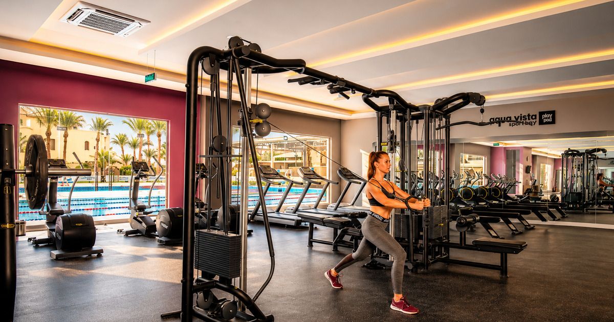 Athlete using cable machine in the resort fitness centre with the Olympic pool visible through floor-to-ceiling windows, Hurghada