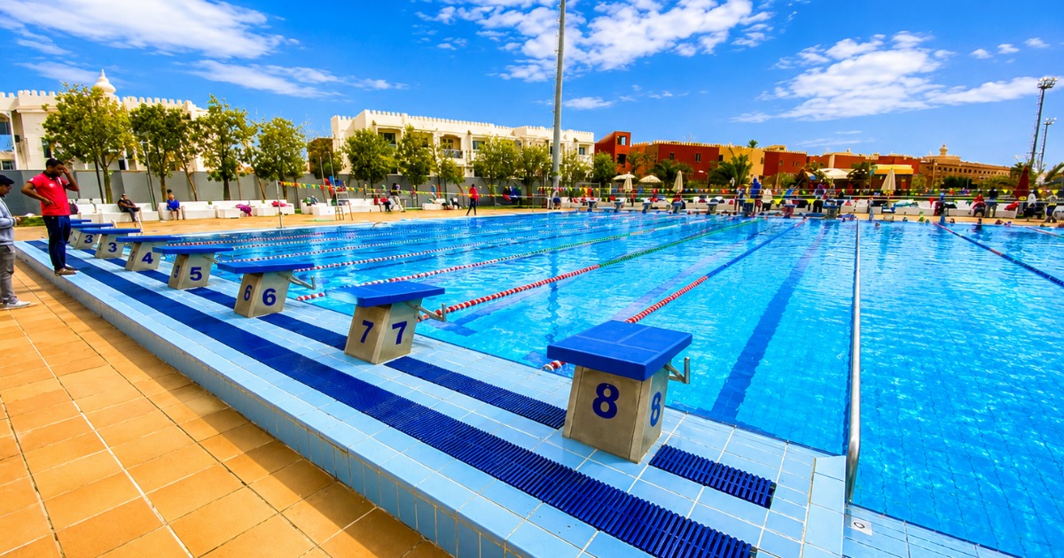 Close-up of competition starting blocks 3 through 8 on the 25m outdoor pool, resort hotel buildings and palm trees visible behind