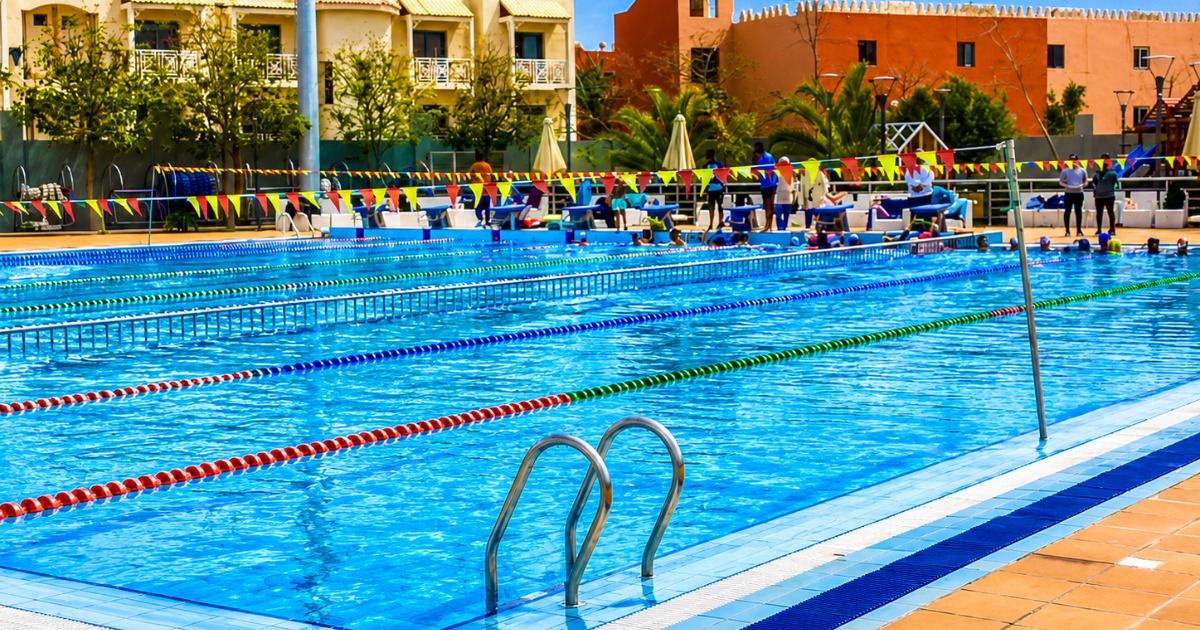 25m competition pool set up for a swim meet with colourful bunting, coaches and athletes on poolside deck, resort buildings in the background, Hurghada