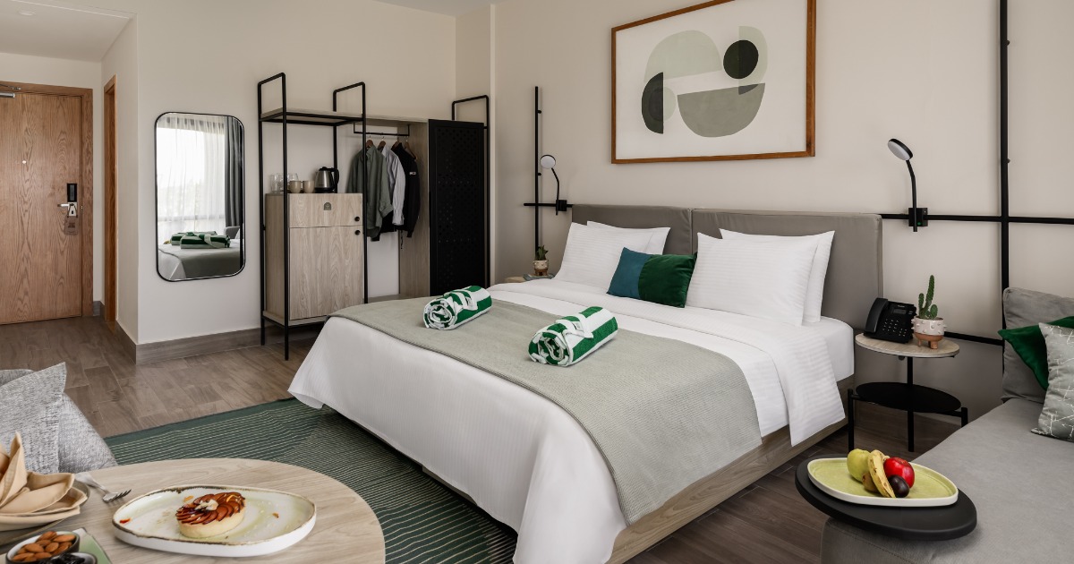 Modern king room at the Soma Bay resort hotel with open-frame wardrobe, abstract wall art, green accent cushions, and breakfast tray on the table