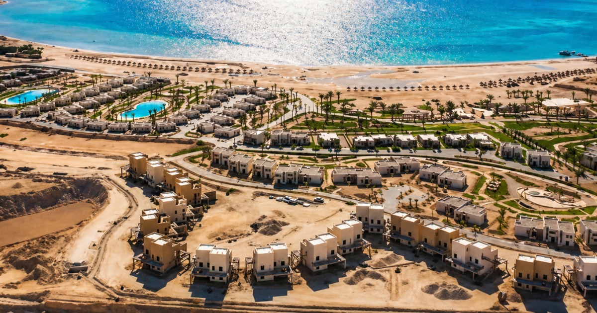 Aerial view of Soma Bay resort complex on the Red Sea coast, showing sandy desert, palm-lined villa compounds, turquoise water, and beach parasols