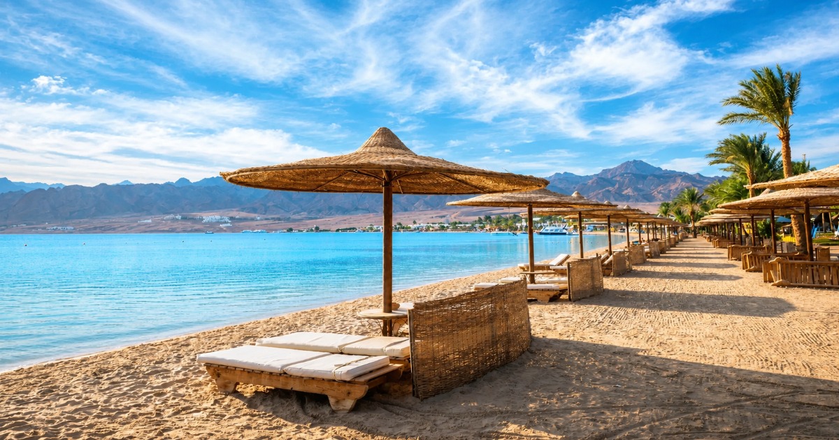 Sandy Red Sea beach with straw umbrellas and sun loungers, calm turquoise water and mountains in the background
