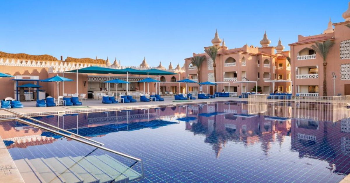 Quiet resort leisure pool with blue sun loungers and umbrellas, Moorish-style hotel buildings reflected in the water