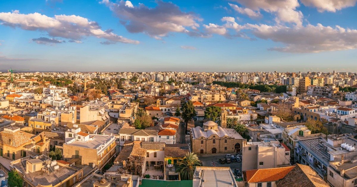 Panoramic aerial view of Nicosia old town with terracotta rooftops, historic stone church, and modern cityscape under a blue sky