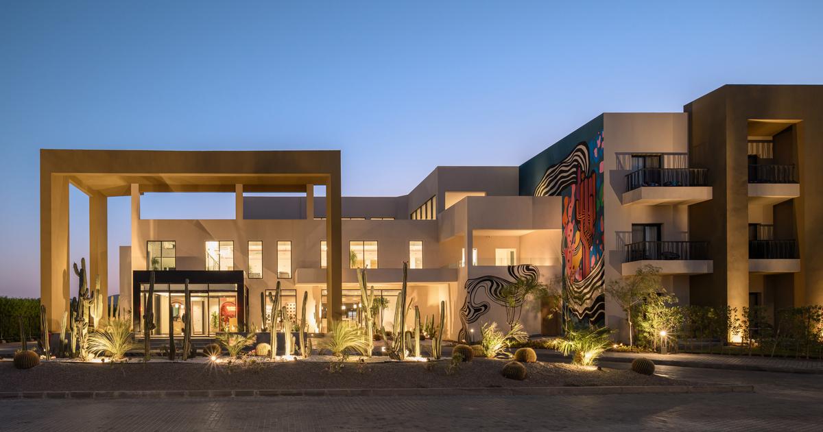 Hotel exterior at dusk featuring desert landscaping with cacti, dramatic lighting, and a bold mural on the facade