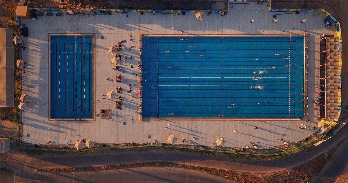 Aerial sunset view of two outdoor swimming pools at a sports complex, with athletes gathered at poolside