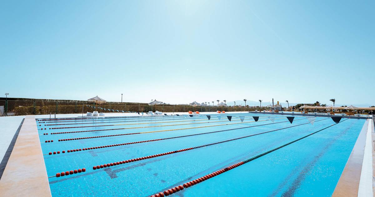 Wide-angle view of an outdoor competition swimming pool with red and black lane dividers under bright sunlight