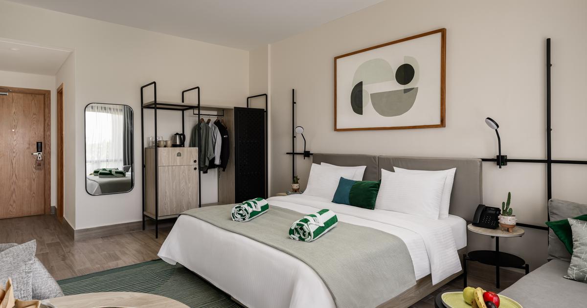Spacious hotel double room with king-size bed, open wardrobe, abstract wall art, and fruit bowl on the side table