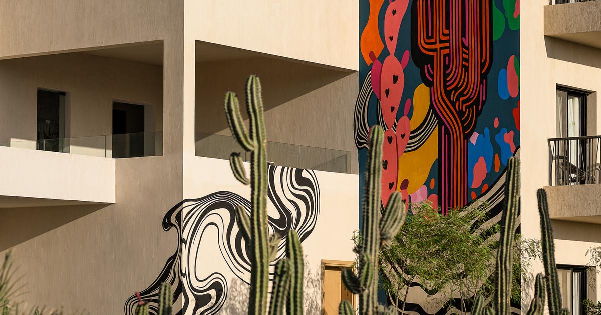 Hotel building exterior by day with tall cacti in the foreground and a bold colourful mural spanning the facade