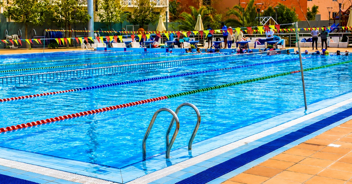 50m competition pool at Hurghada multi-sport complex during an active training session, with swimmers in the water, coaches on deck, and colourful competition bunting