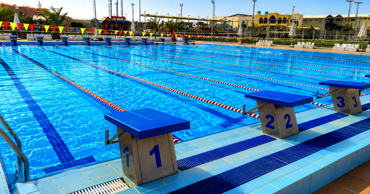 50m outdoor Olympic competition pool at Hurghada sports complex, view from lane 1 end showing full pool length with competition bunting and resort buildings