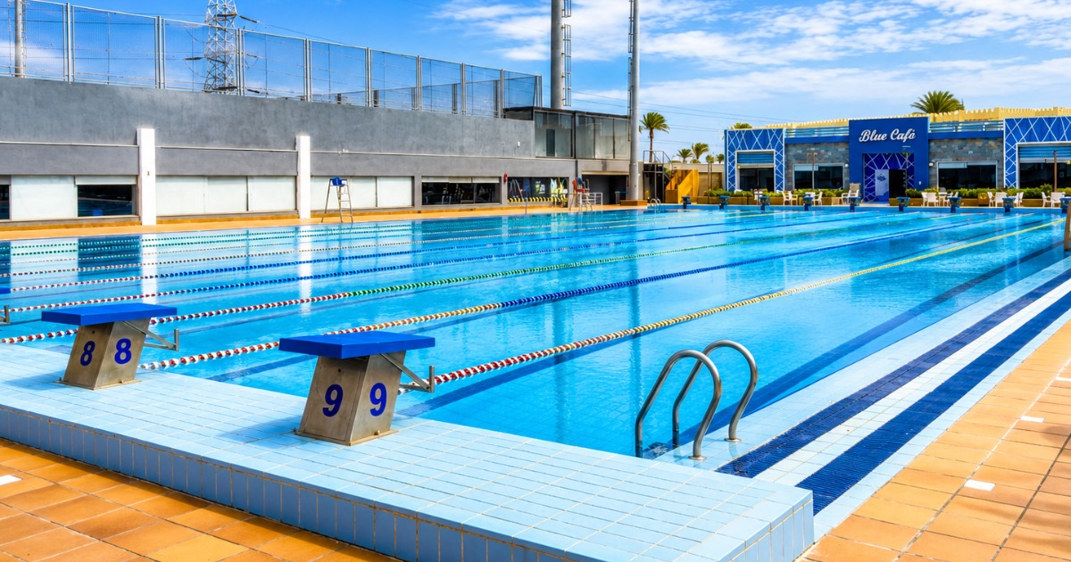 50m outdoor competition pool at Hurghada multi-sport complex, lanes 8–9 end, with Blue Café and sports complex facilities visible in the background
