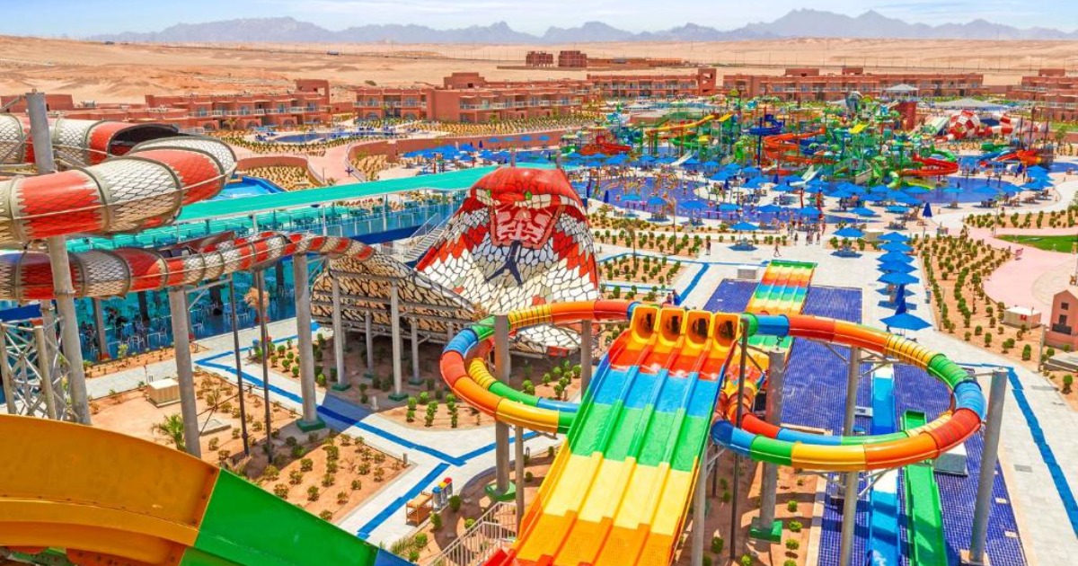 Wide aerial view of the Hurghada resort complex showing water park slides, leisure pools, and terracotta resort buildings against the desert horizon