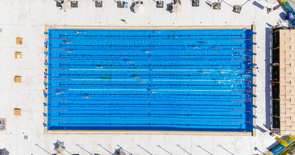 Soma Bay 50m Olympic pool — top-down aerial with swimmers in all lanes during training